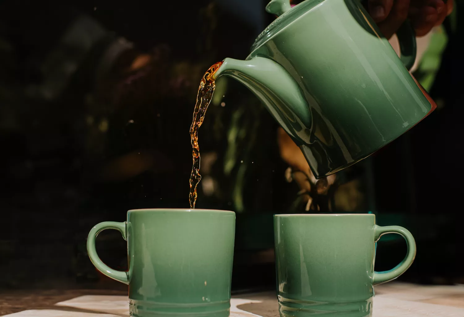 A close-up shot of tea being poured into two ceramic mugs, suggesting a moment of calm social connection.