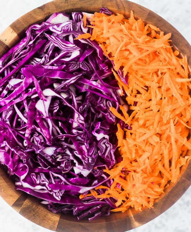 Finely shredded red cabbage and carrots served in a rustic wooden bowl.