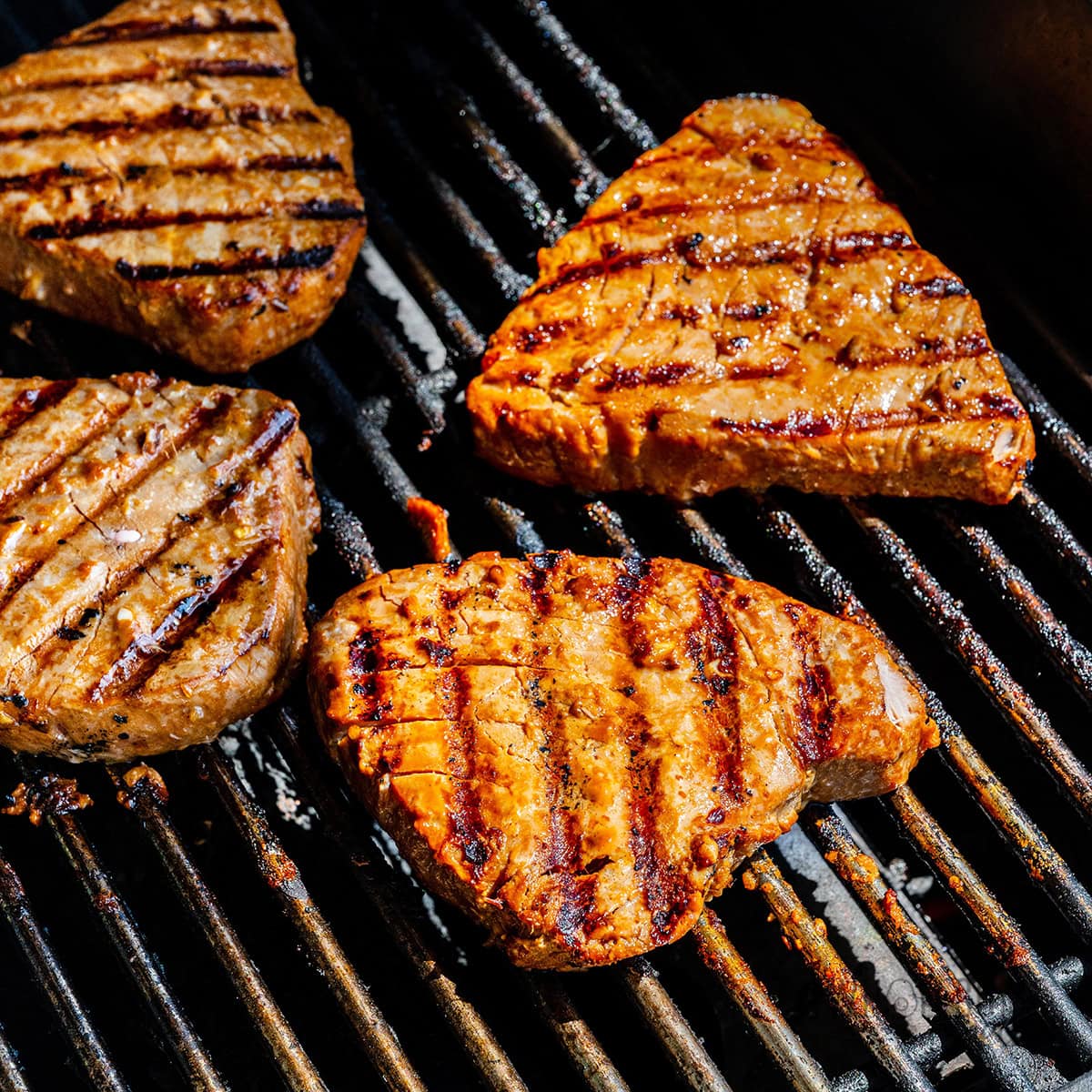 A thick tuna steak being cooked on hot metal grill grates with visible searing.