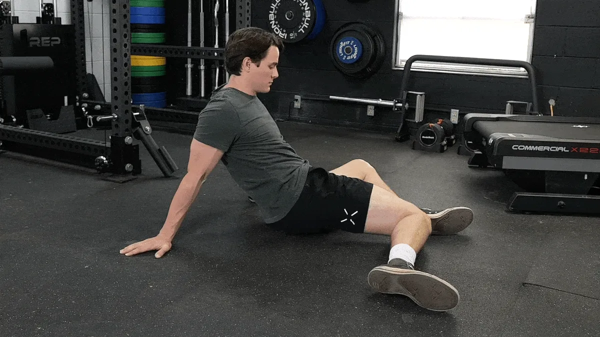 A person sitting on an exercise mat performing a 90/90 hip rotation drill.