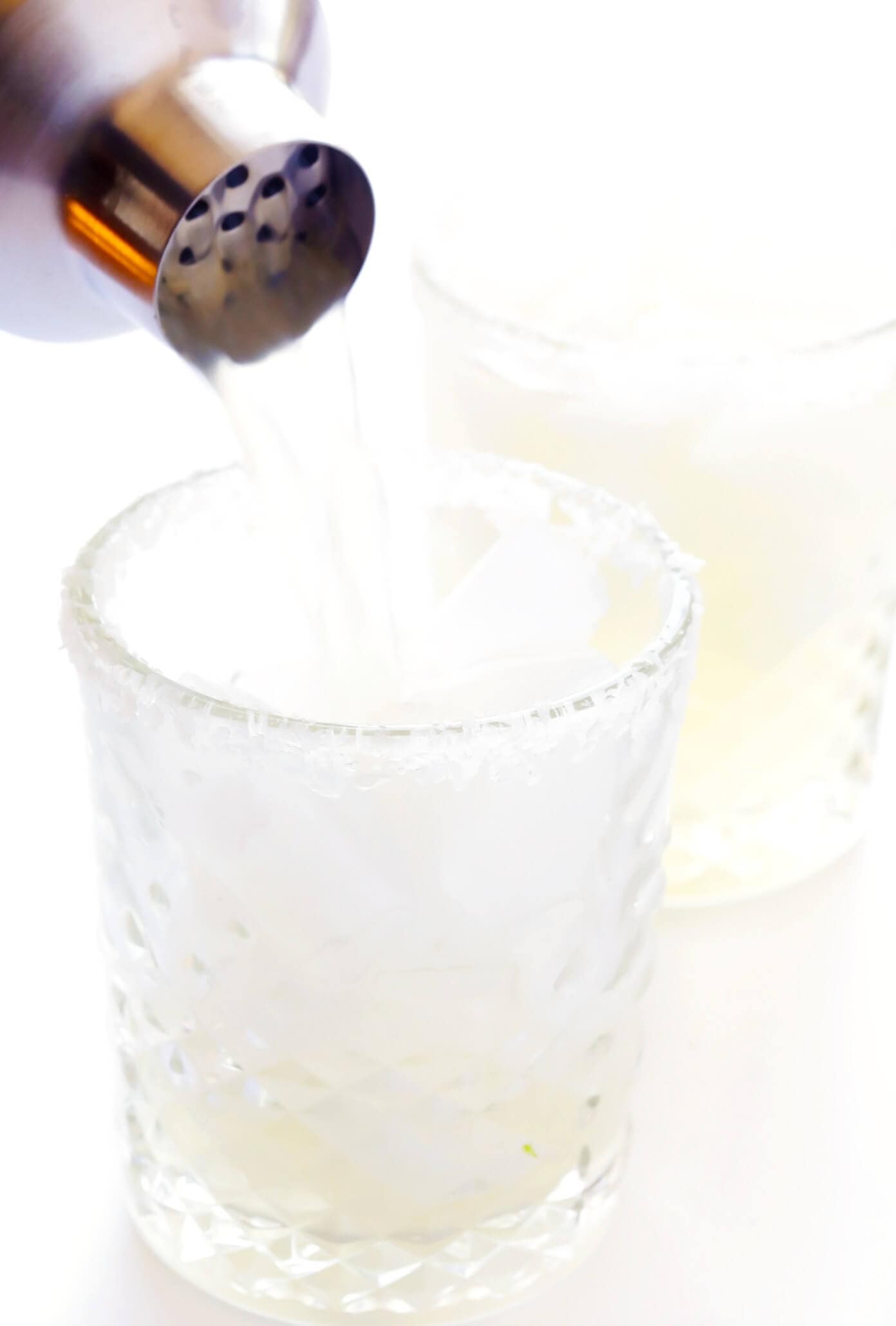 A cocktail being poured through a metal strainer into a glass filled with fresh ice.