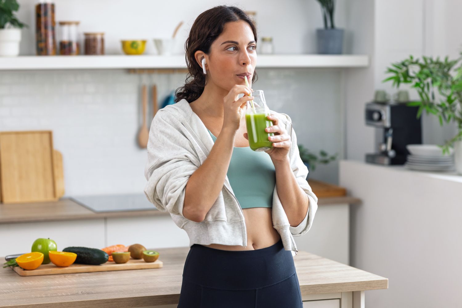 A person in athletic wear drinking a smoothie in a kitchen, representing post-workout recovery.