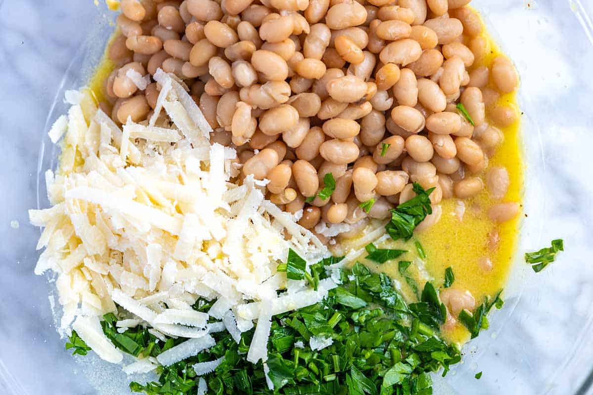 Mixing white beans into a bowl containing lemon dressing and fresh herbs.