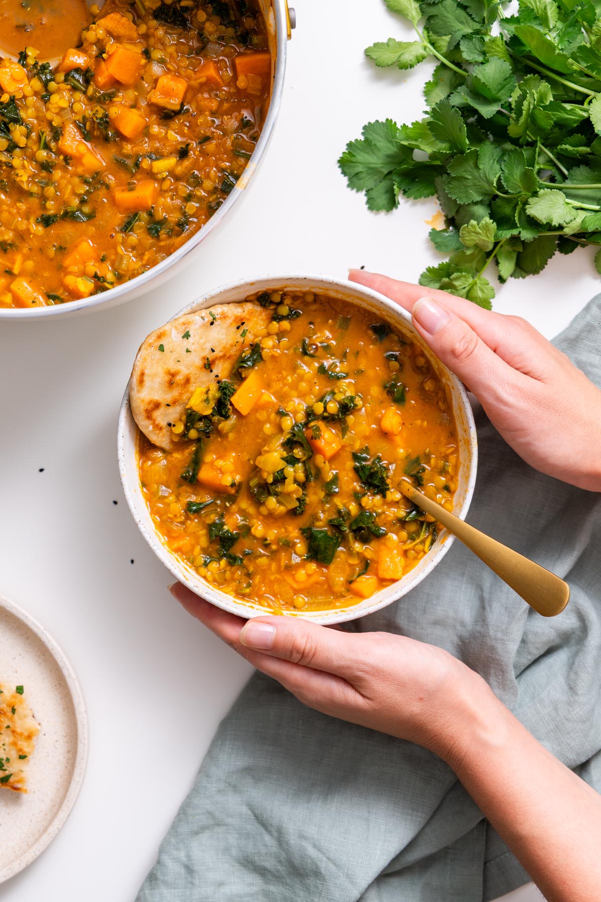 A woman holding a warm bowl of sweet potato lentil stew with a side of naan.