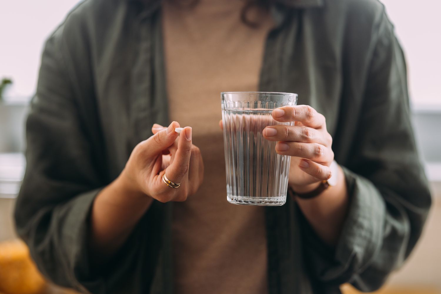 A woman taking a supplement capsule with a glass of water to support her neurovascular health.