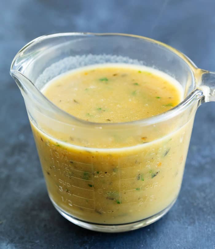 A glass measuring cup filled with thick, brown chicken gravy placed on a blue surface.