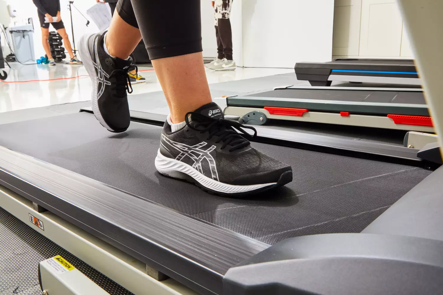 A person walking on a treadmill in a clinical lab environment for gait analysis.
