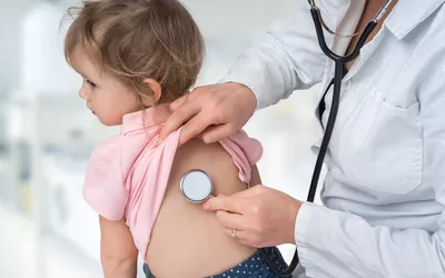 A pediatrician performing a medical checkup on a young child using a stethoscope.