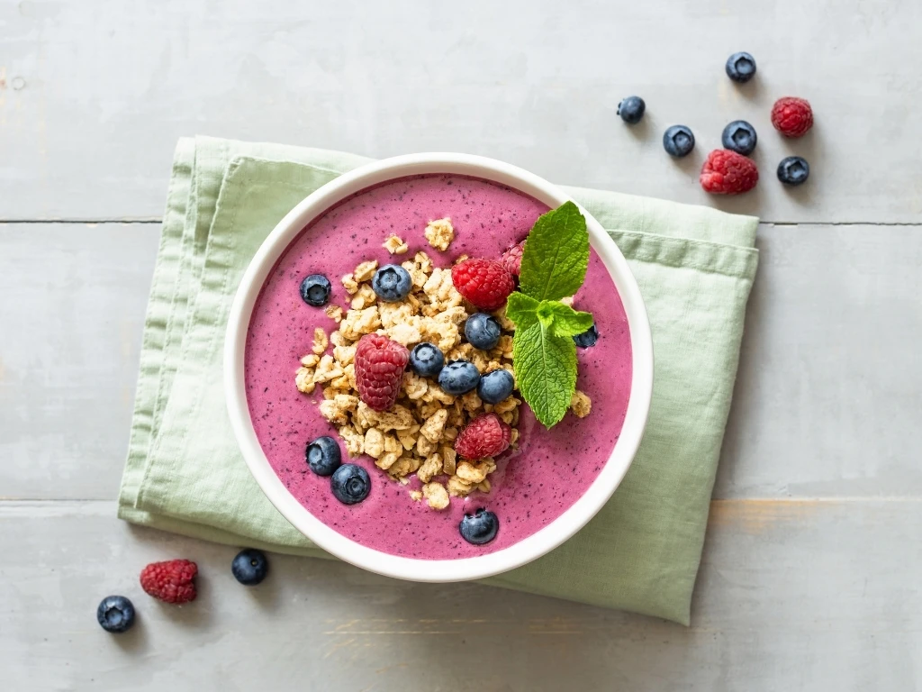 Fresh yogurt and berry smoothie bowl topped with various nuts and granola.