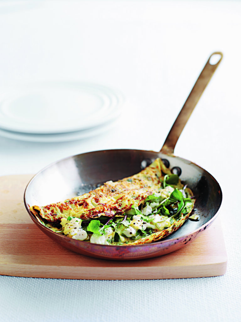 A fresh omelette garnished with green rocket leaves and goat cheese on a white plate.