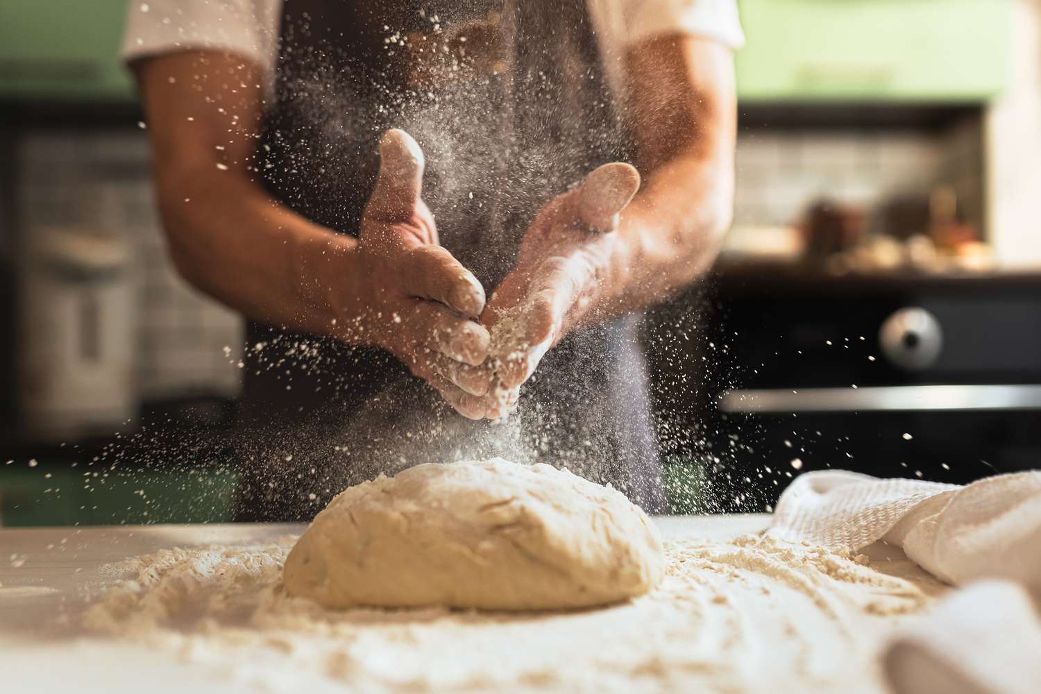A baker dusting flour over dough, showing flour particles suspended in the air.