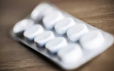 A close-up of white oval pills in a silver foil blister pack on a wooden surface.