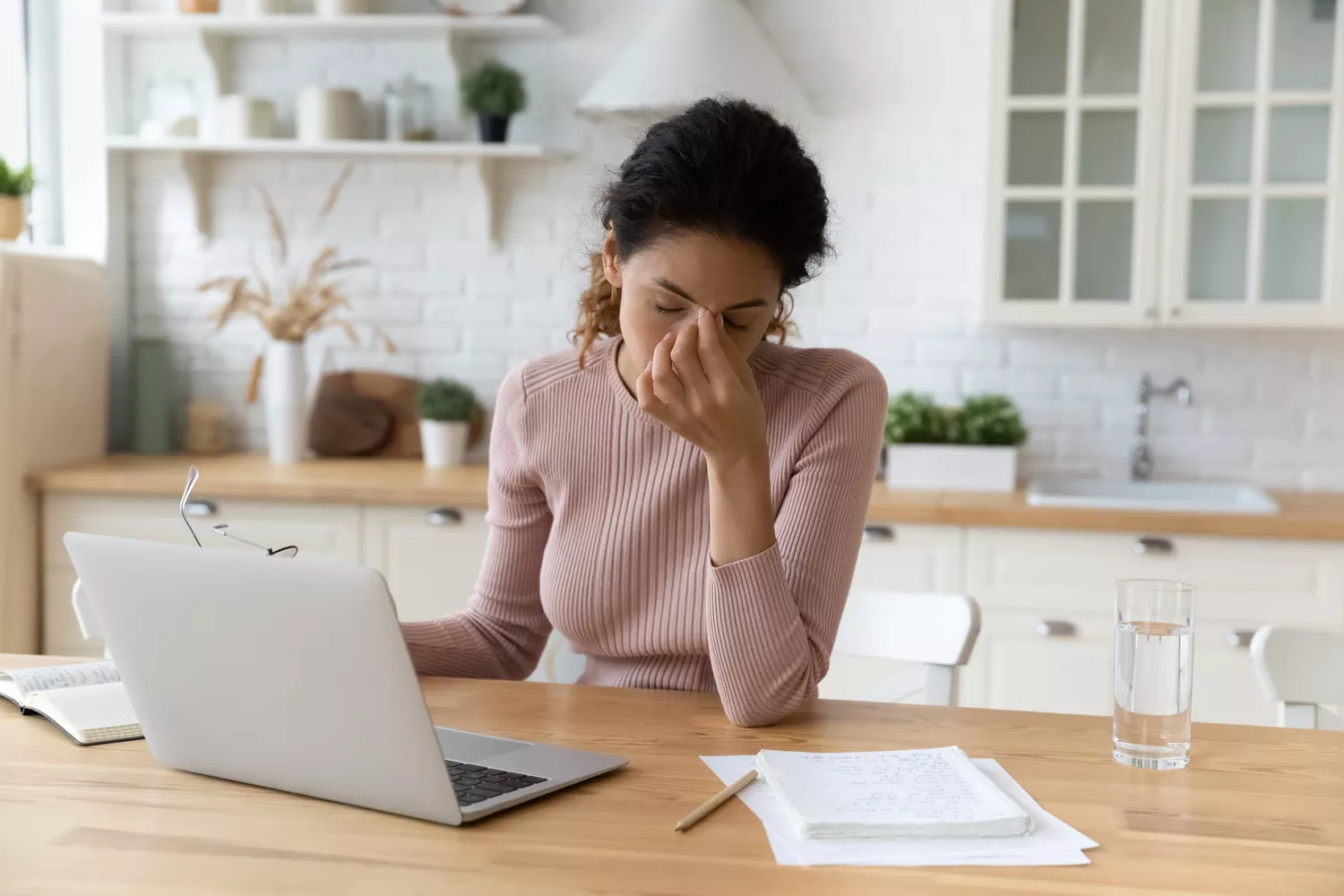 A woman at a laptop looking stressed and pinching the bridge of her nose.