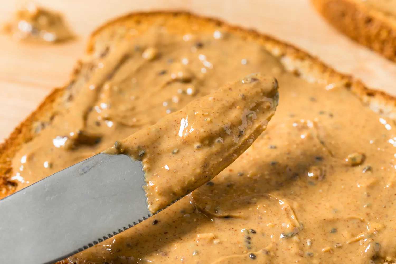 Nut butter spread onto a slice of whole grain toast next to a knife.