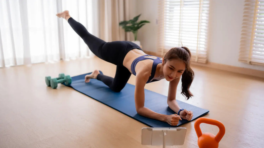 A woman performing a gentle stretching exercise on a yoga mat in a bright room.