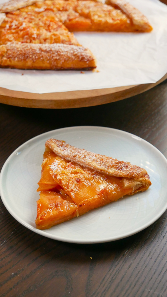 Vertical full-length shot of a whole baked persimmon galette showcasing its concentric fruit pattern and caramelized edges.