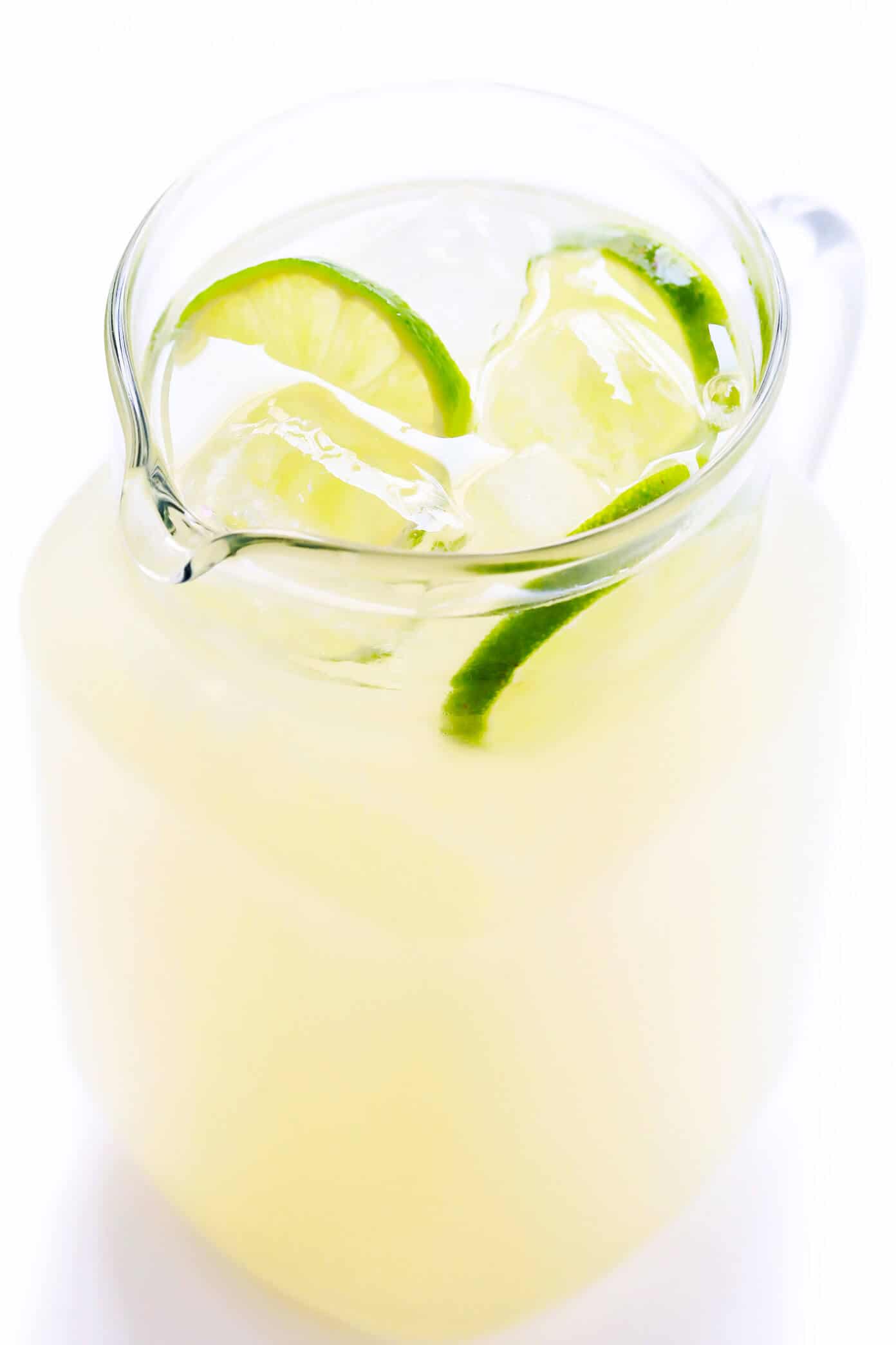 A glass pitcher filled with a pale yellow margarita mixture and floating fresh lime slices.