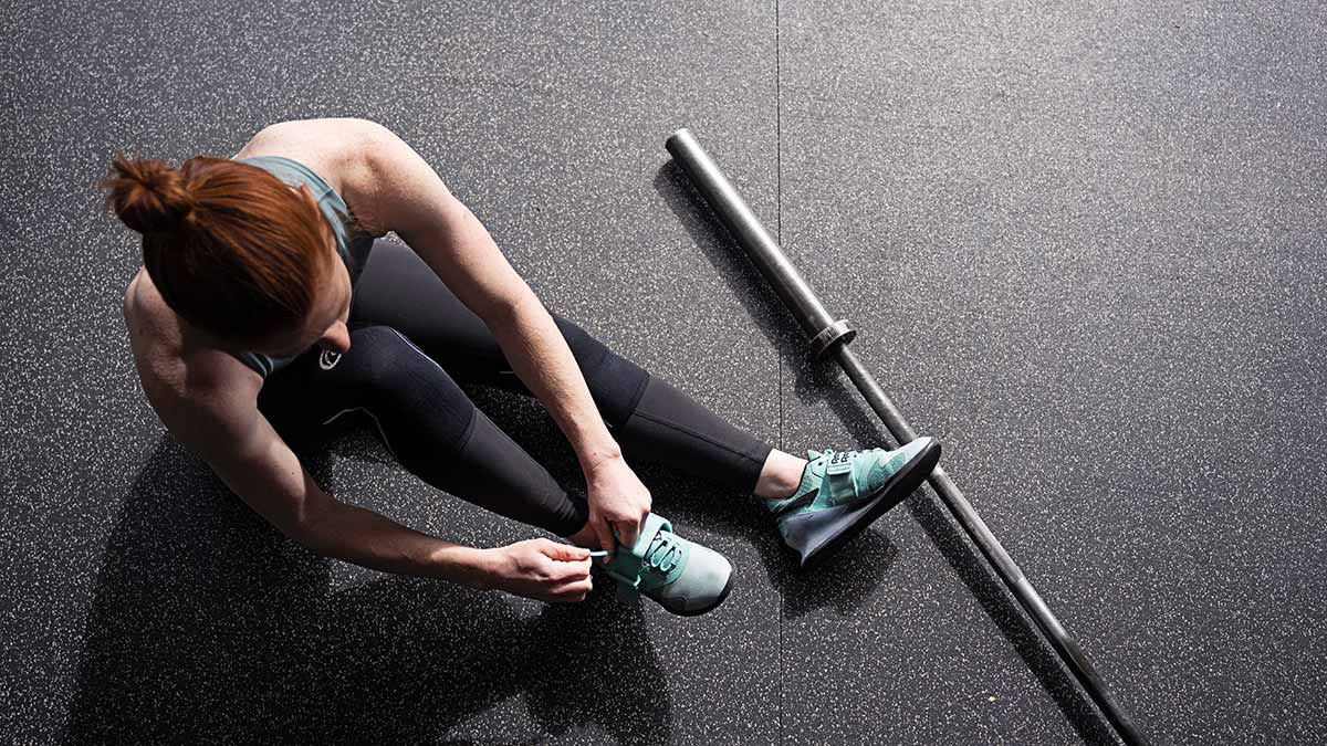 A woman sitting on a bench tying her athletic shoes in a gym.