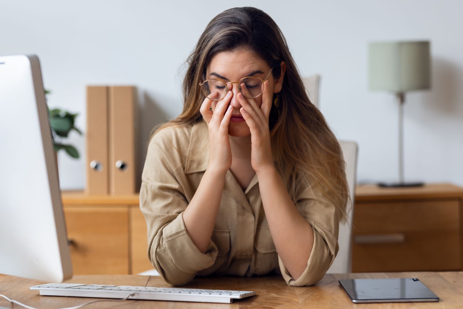 A woman looking exhausted and overwhelmed while working at her desk.