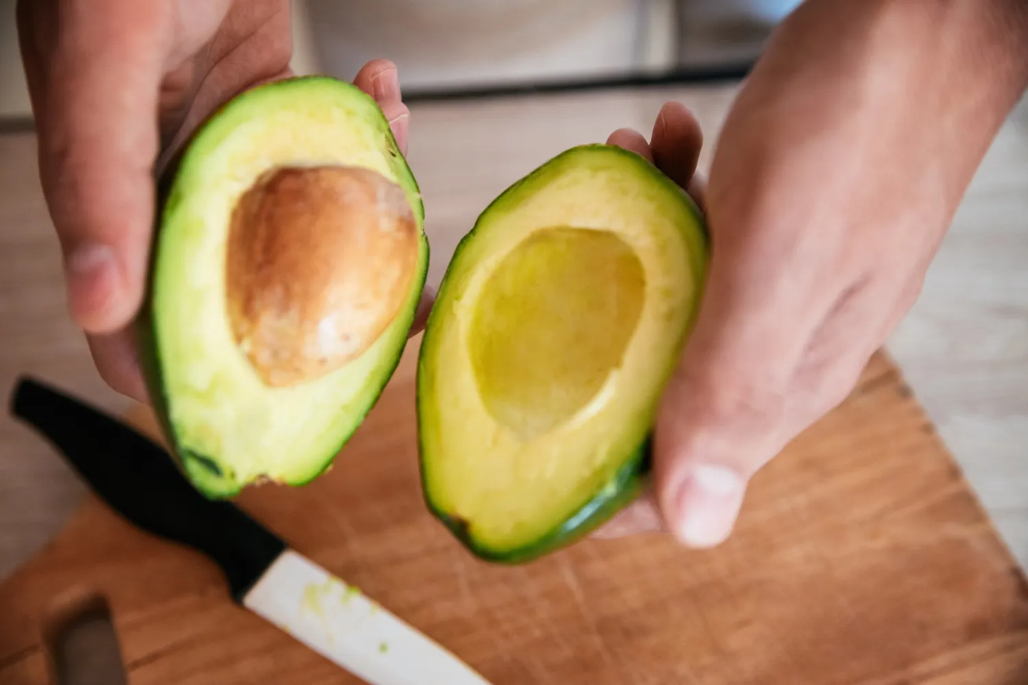 A person holding two halves of a fresh avocado.