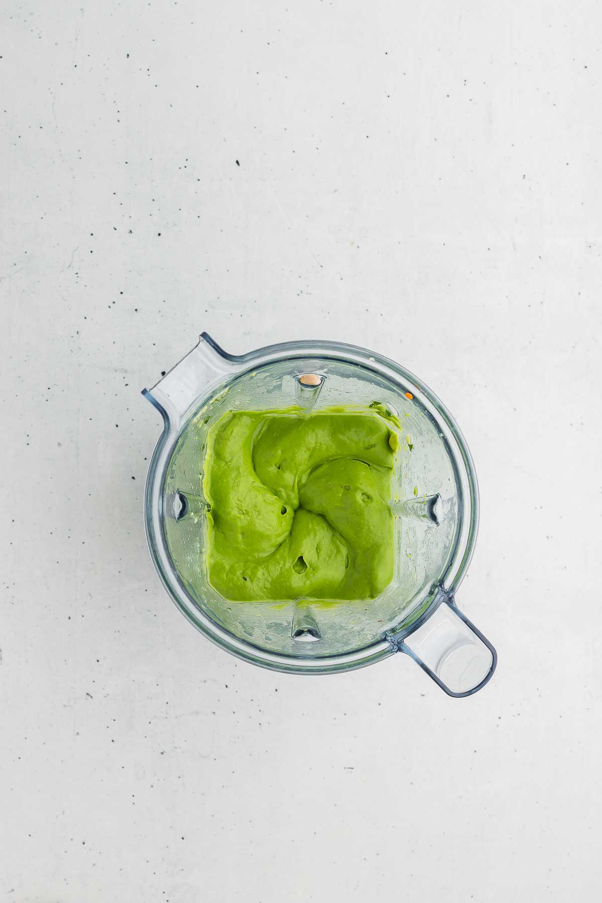 A high-speed blender processing a bright green mixture of avocado and herbs.
