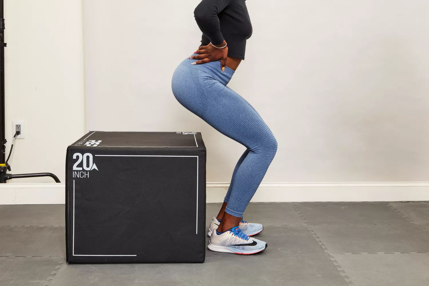 A woman performing a box squat in a gym to test the coverage of her leggings.