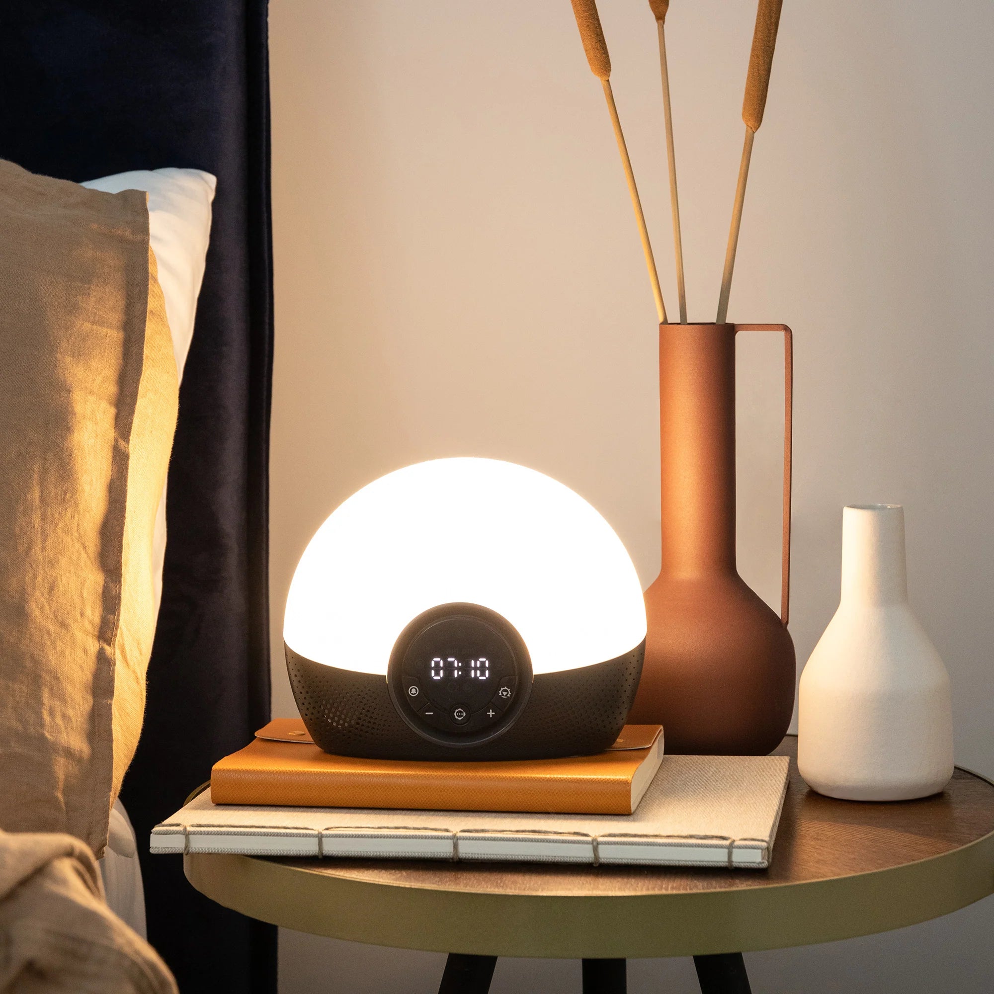 A Lumie sunrise alarm clock emitting a warm, soft orange glow on a bedside table.